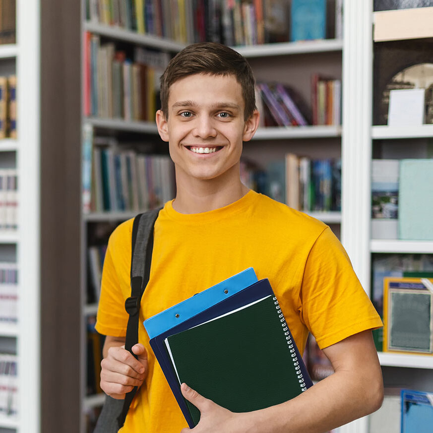 Excited caucasian student posing next to bookshelves in campus library, free space